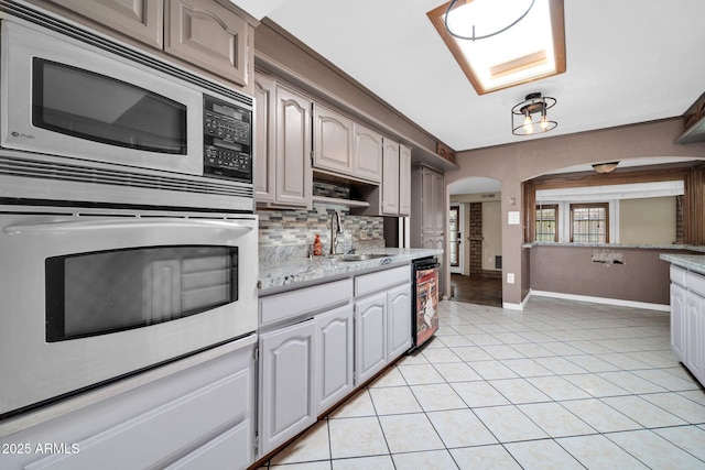 6217 W Orange Dr, Glendale, AZ 85301 - kitchen with appliances with stainless steel finishes, arched walkways, decorative backsplash, light tile patterned floors, and light stone countertops