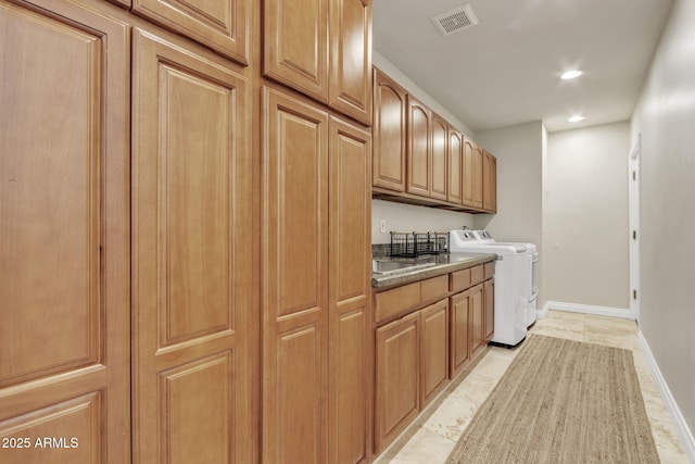 clothes washing area featuring separate washer and dryer, light tile patterned floors, and cabinets