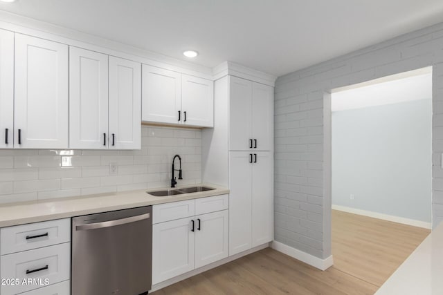 kitchen with dishwasher, light countertops, light wood-style flooring, white cabinets, and a sink