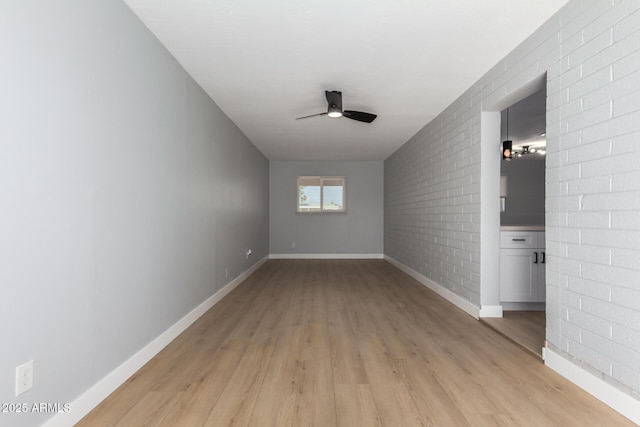 spare room featuring ceiling fan, baseboards, light wood-style flooring, and brick wall