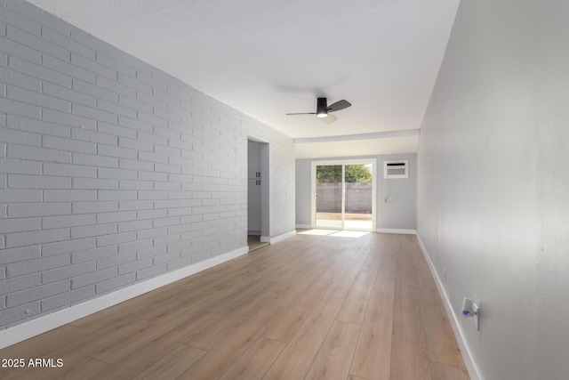 unfurnished room featuring baseboards, brick wall, light wood finished floors, ceiling fan, and an AC wall unit