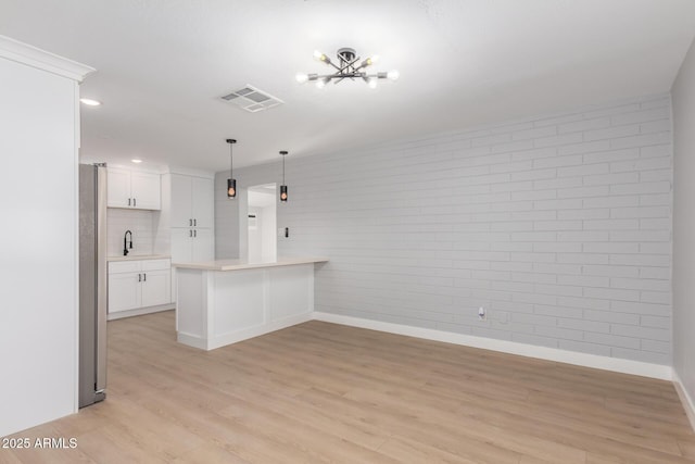 kitchen with visible vents, light wood finished floors, a peninsula, light countertops, and white cabinets