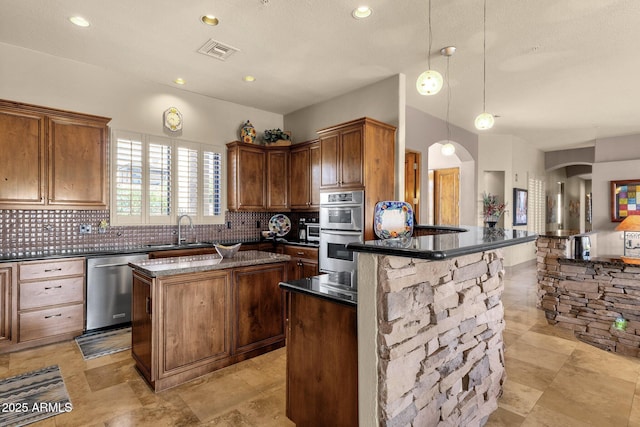 kitchen featuring arched walkways, decorative backsplash, stainless steel appliances, a kitchen island, and a sink