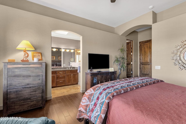 bedroom featuring dark wood-style flooring, ensuite bathroom, a sink, and arched walkways