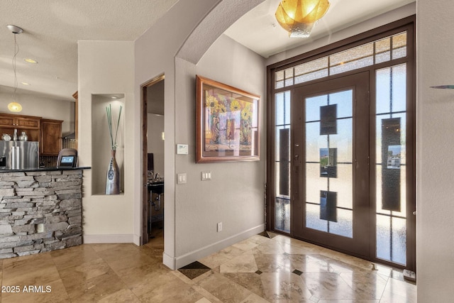 foyer with light tile patterned floors, arched walkways, a textured ceiling, and baseboards