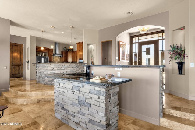 kitchen featuring arched walkways, stainless steel fridge with ice dispenser, dark countertops, visible vents, and wall chimney exhaust hood