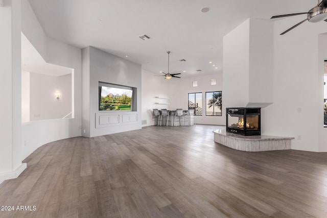 unfurnished living room with ceiling fan, a multi sided fireplace, and light wood-type flooring