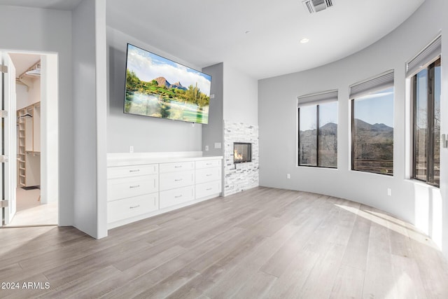 unfurnished living room with a stone fireplace and light wood-type flooring