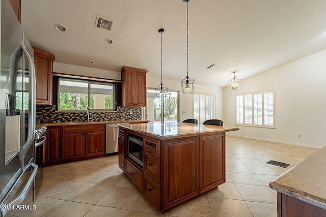 kitchen featuring a kitchen island, pendant lighting, a chandelier, stainless steel appliances, and plenty of natural light