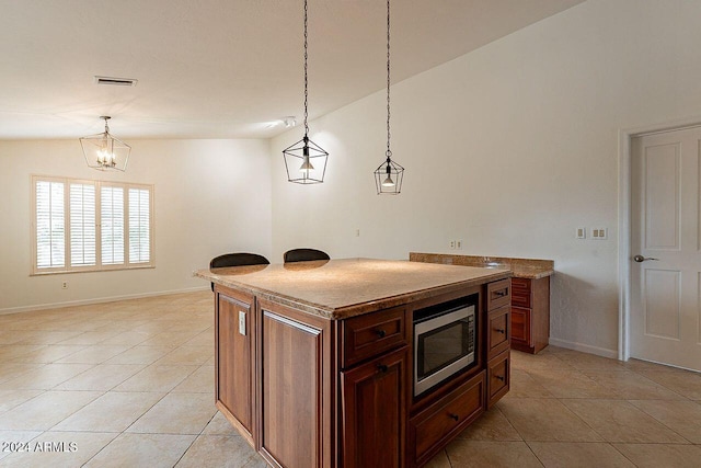 kitchen featuring light tile patterned floors, hanging light fixtures, stainless steel microwave, a notable chandelier, and a kitchen island