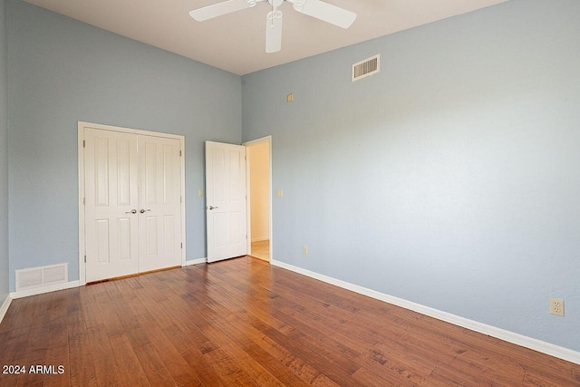 unfurnished bedroom featuring a towering ceiling, wood-type flooring, a closet, and ceiling fan