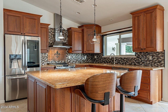 kitchen featuring light tile patterned flooring, a kitchen island, appliances with stainless steel finishes, decorative light fixtures, and light stone counters