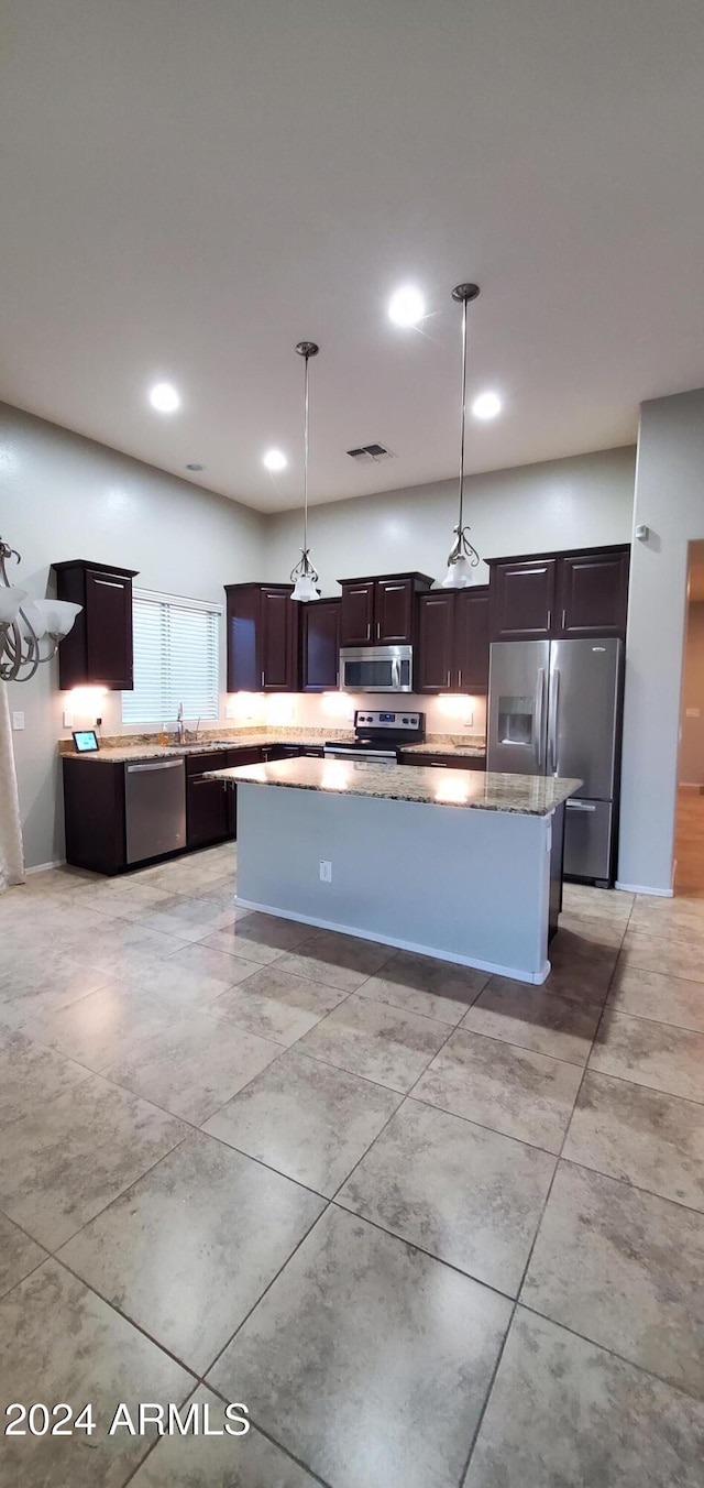 kitchen with pendant lighting, dark brown cabinets, stainless steel appliances, light stone counters, and a kitchen island