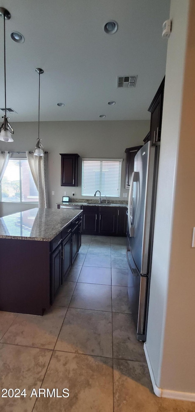 kitchen featuring pendant lighting, sink, stainless steel fridge, light stone countertops, and dark brown cabinets