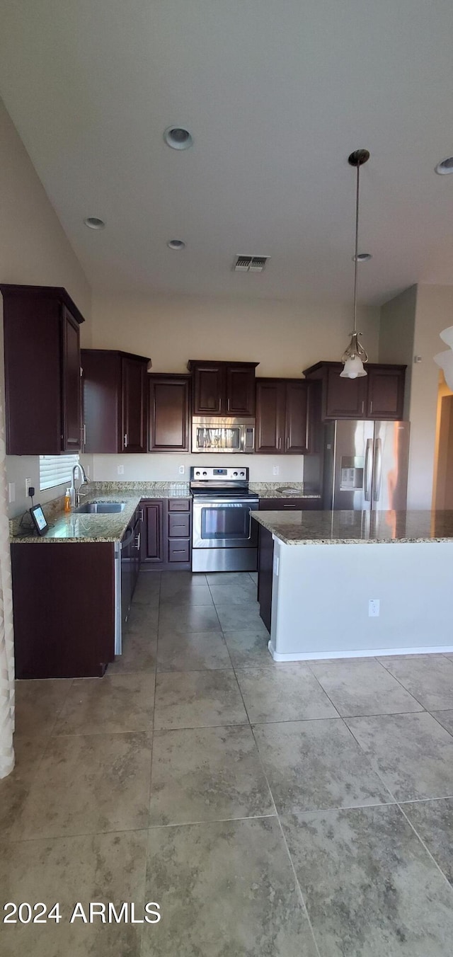 kitchen featuring decorative light fixtures, sink, dark brown cabinetry, stainless steel appliances, and light stone countertops