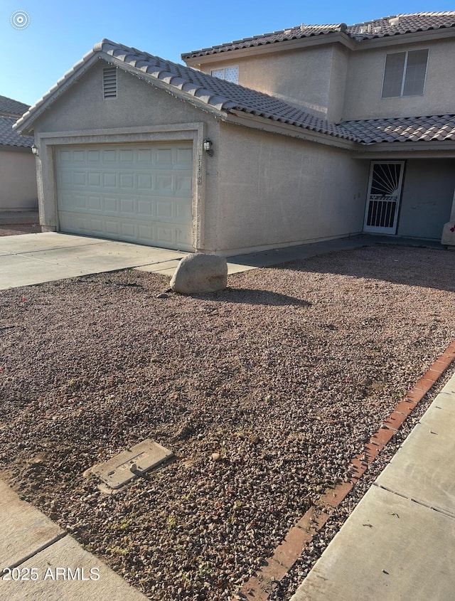 view of side of property with an attached garage, stucco siding, a tiled roof, and driveway