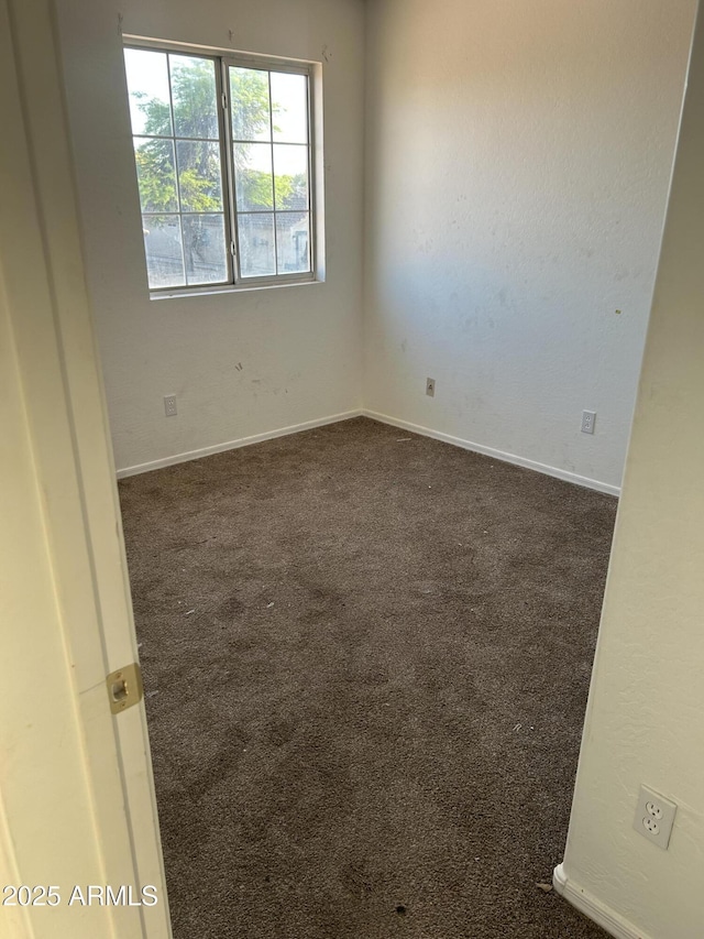 unfurnished room featuring baseboards and dark colored carpet