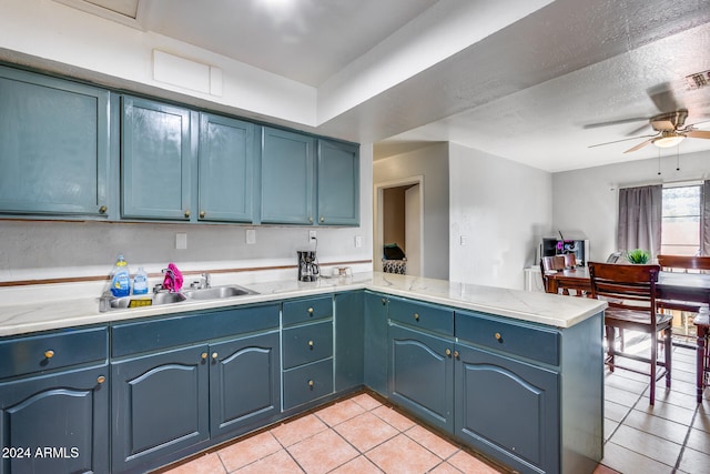 kitchen featuring blue cabinetry, kitchen peninsula, sink, and light tile patterned flooring