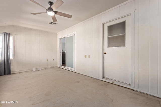 unfurnished bedroom with lofted ceiling, wood walls, and ceiling fan