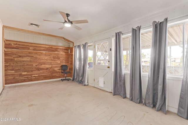 unfurnished room featuring lofted ceiling, wood walls, ceiling fan, and a wealth of natural light