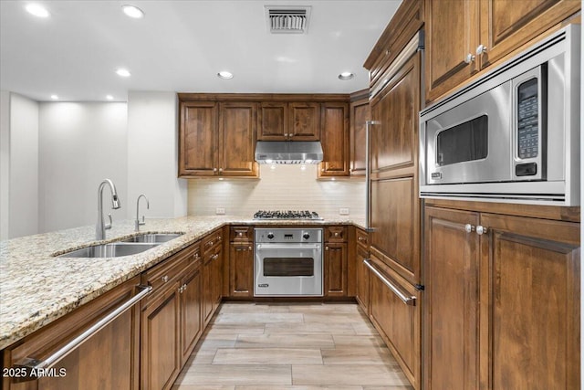 kitchen featuring sink, light stone counters, light hardwood / wood-style flooring, appliances with stainless steel finishes, and decorative backsplash