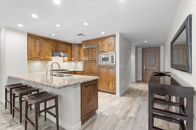 kitchen featuring sink, light hardwood / wood-style flooring, stainless steel microwave, kitchen peninsula, and light stone countertops