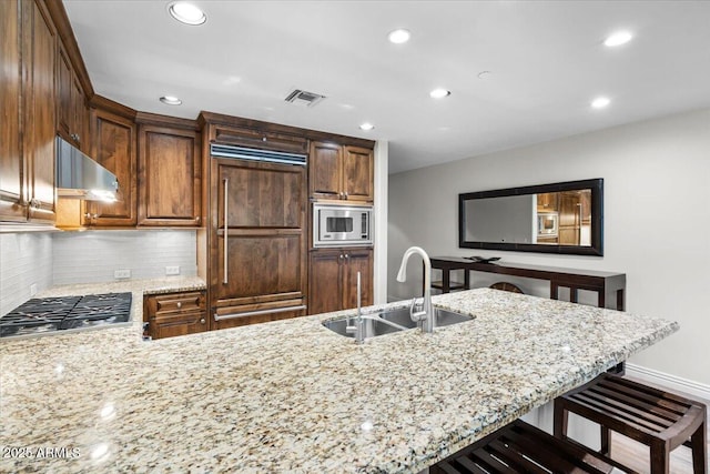 kitchen with light stone countertops, sink, built in appliances, and a kitchen breakfast bar