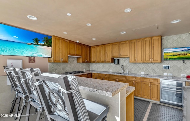 kitchen with a kitchen bar, sink, tasteful backsplash, light tile patterned floors, and stainless steel gas stovetop