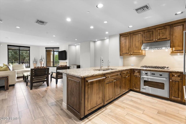 kitchen featuring sink, stainless steel appliances, light stone countertops, light hardwood / wood-style floors, and backsplash