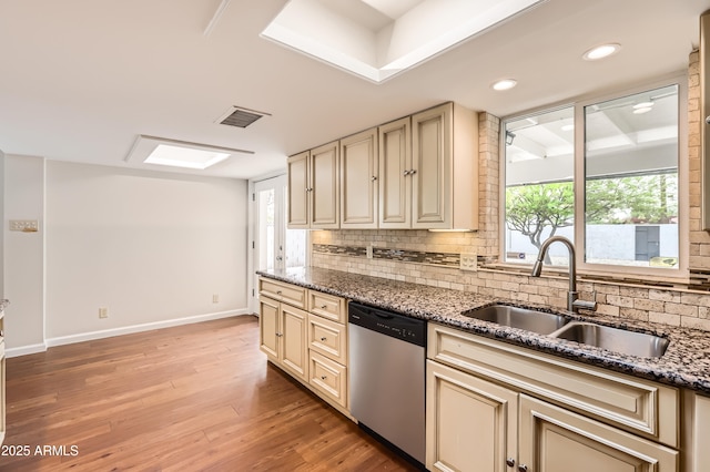 kitchen with decorative backsplash, a sink, baseboards, dishwasher, and cream cabinets