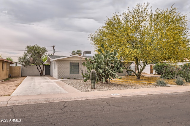obstructed view of property with brick siding, concrete driveway, and fence