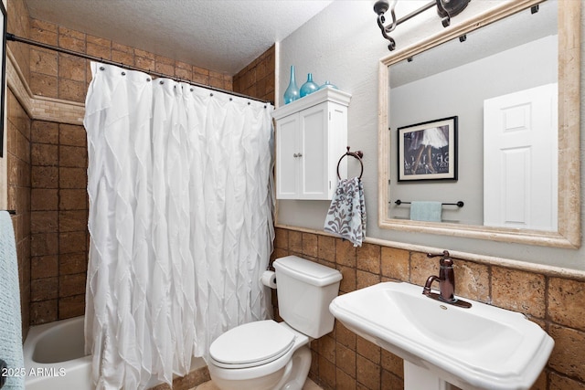 full bathroom with shower / tub combo with curtain, sink, tile walls, toilet, and a textured ceiling