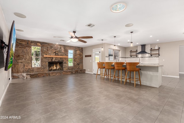 kitchen with wall chimney range hood, ceiling fan, a fireplace, decorative light fixtures, and kitchen peninsula