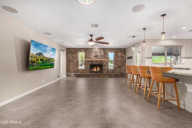 tiled living room featuring a fireplace, ceiling fan, and sink