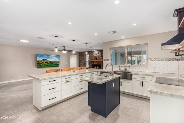 kitchen featuring light stone countertops, black electric cooktop, pendant lighting, white cabinets, and an island with sink