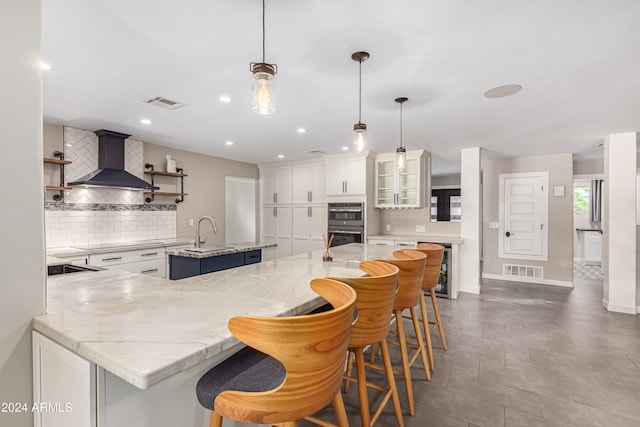 kitchen with white cabinets, an island with sink, decorative light fixtures, and custom range hood