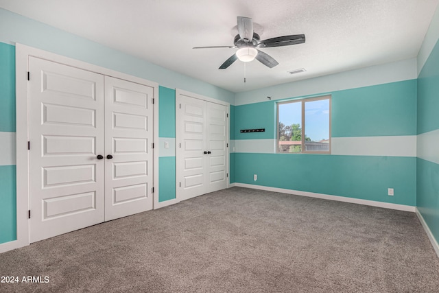 unfurnished bedroom with multiple closets, ceiling fan, carpet floors, and a textured ceiling