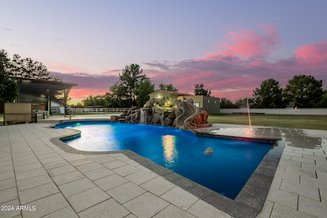 pool at dusk with pool water feature, a patio area, and a water slide