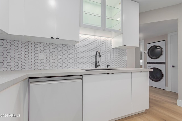 kitchen with dishwasher, a sink, stacked washer / drying machine, white cabinets, and light countertops