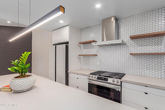 kitchen featuring stainless steel gas range oven, wall chimney range hood, open shelves, freestanding refrigerator, and light countertops
