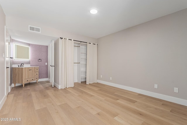unfurnished bedroom featuring light wood-style flooring, baseboards, and a sink