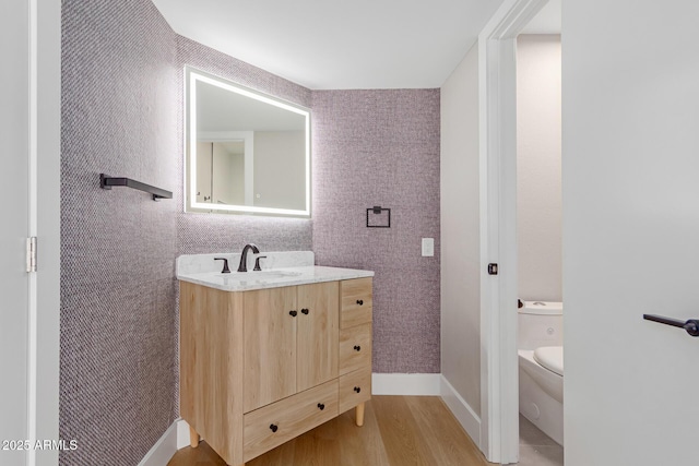 bathroom with wood finished floors, toilet, vanity, and baseboards