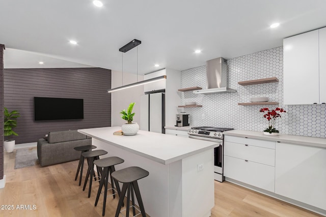 kitchen featuring gas range, wall chimney range hood, open shelves, freestanding refrigerator, and a breakfast bar area