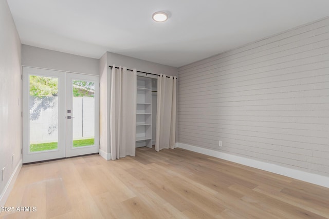 unfurnished bedroom featuring baseboards, french doors, light wood-style floors, access to exterior, and wood walls