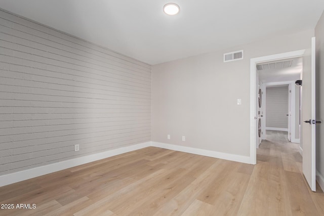 spare room with baseboards, light wood-style floors, and stacked washer / dryer