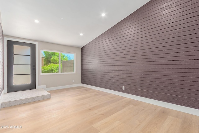 unfurnished living room with vaulted ceiling, light wood-style flooring, recessed lighting, baseboards, and wooden walls