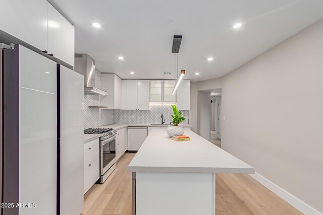 kitchen featuring stainless steel gas range oven, wall chimney exhaust hood, dishwashing machine, light wood-style floors, and recessed lighting