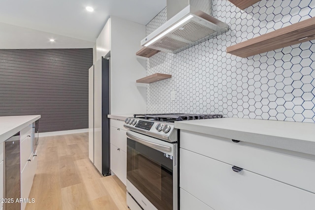 kitchen with stainless steel range with gas cooktop, open shelves, wall chimney range hood, freestanding refrigerator, and white cabinets