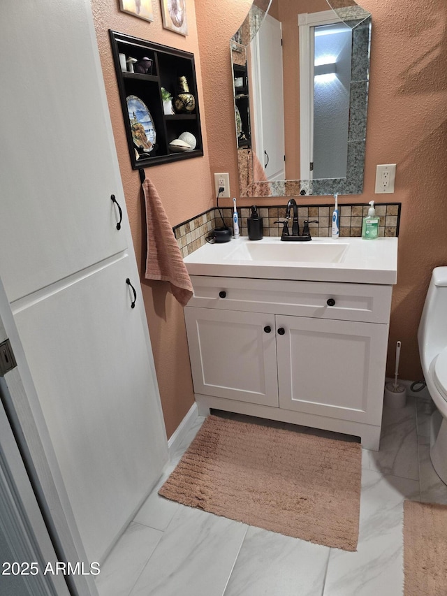 bathroom featuring marble finish floor, vanity, toilet, and backsplash