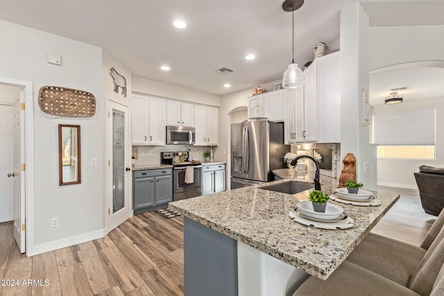 kitchen with sink, appliances with stainless steel finishes, pendant lighting, white cabinets, and light wood-type flooring